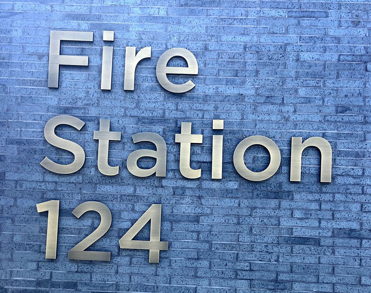 Brushed metal letters reading Fire Station 124 on a dark grey brick wall