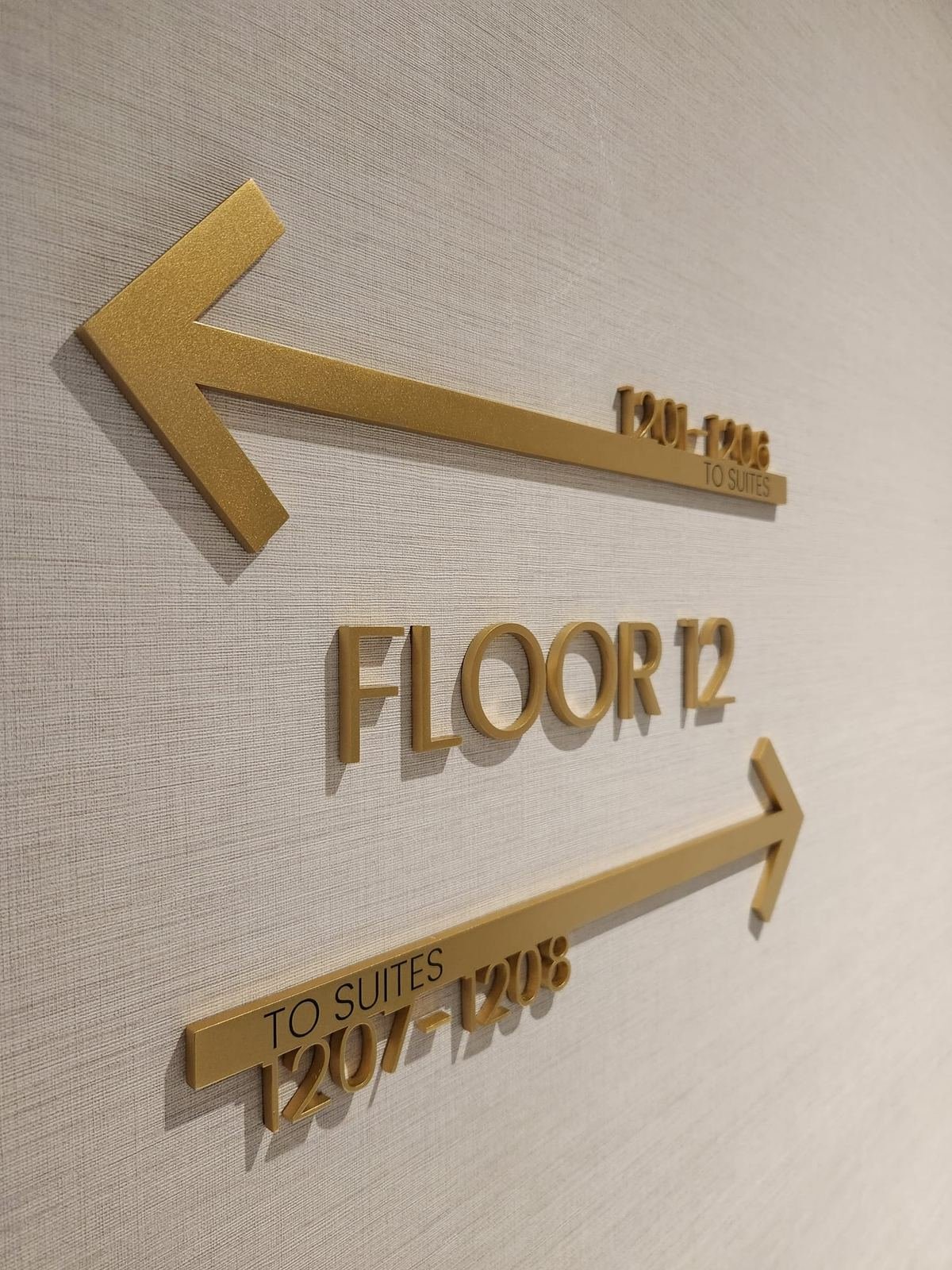 Gold FLOOR 12 letters with arrows pointing to suite numbers on a textured wall
