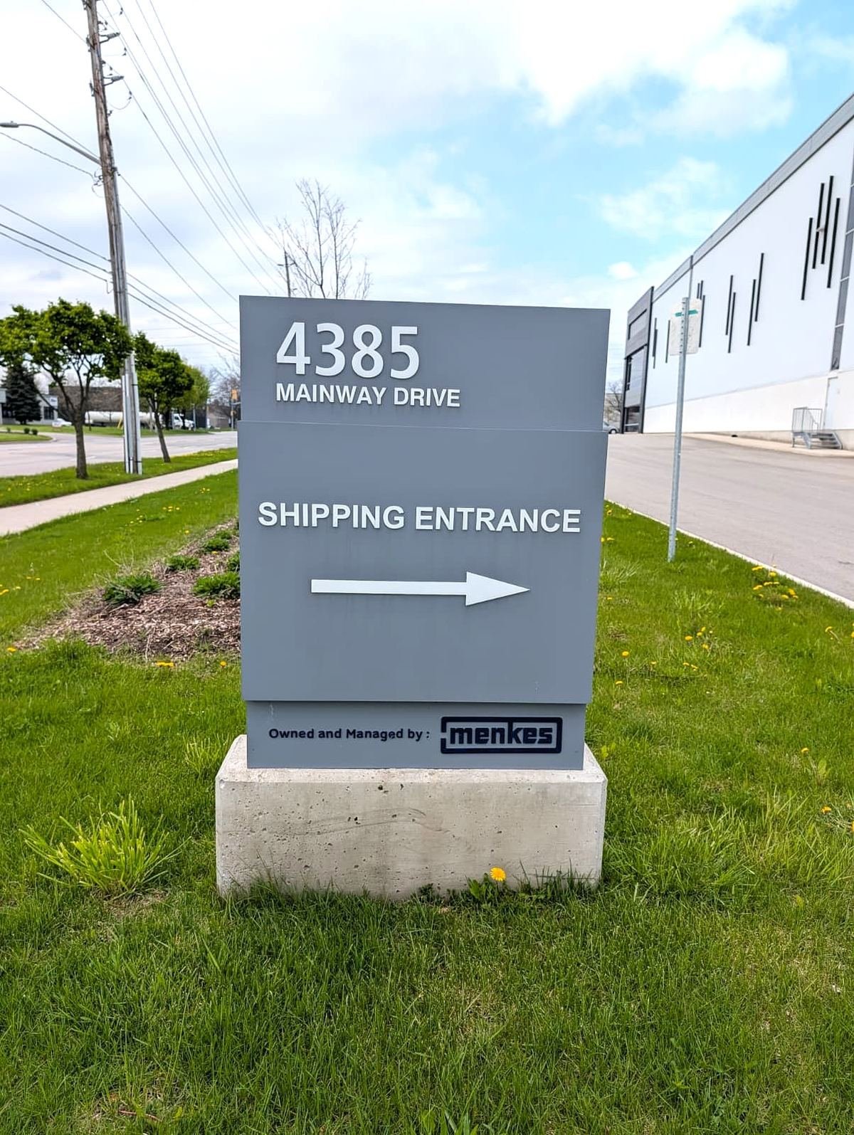 Grey 4385 Mainway Drive shipping entrance sign with an arrow on a concrete base