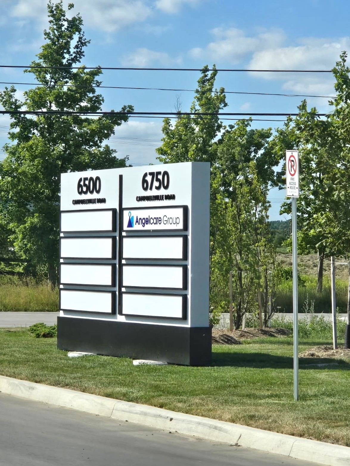 White multi-tenant pylon sign with 6500 and 6750 address numbers and tenant panels on a dark base