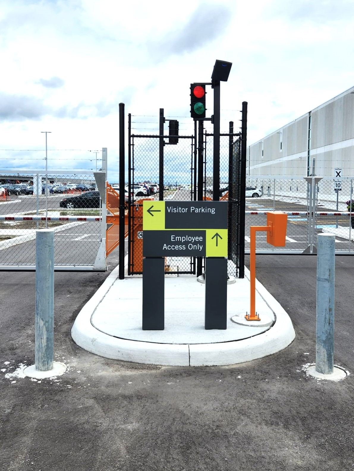 Post-mounted signs on a traffic island pointing to Visitor Parking and Employee Access Only beside a gate