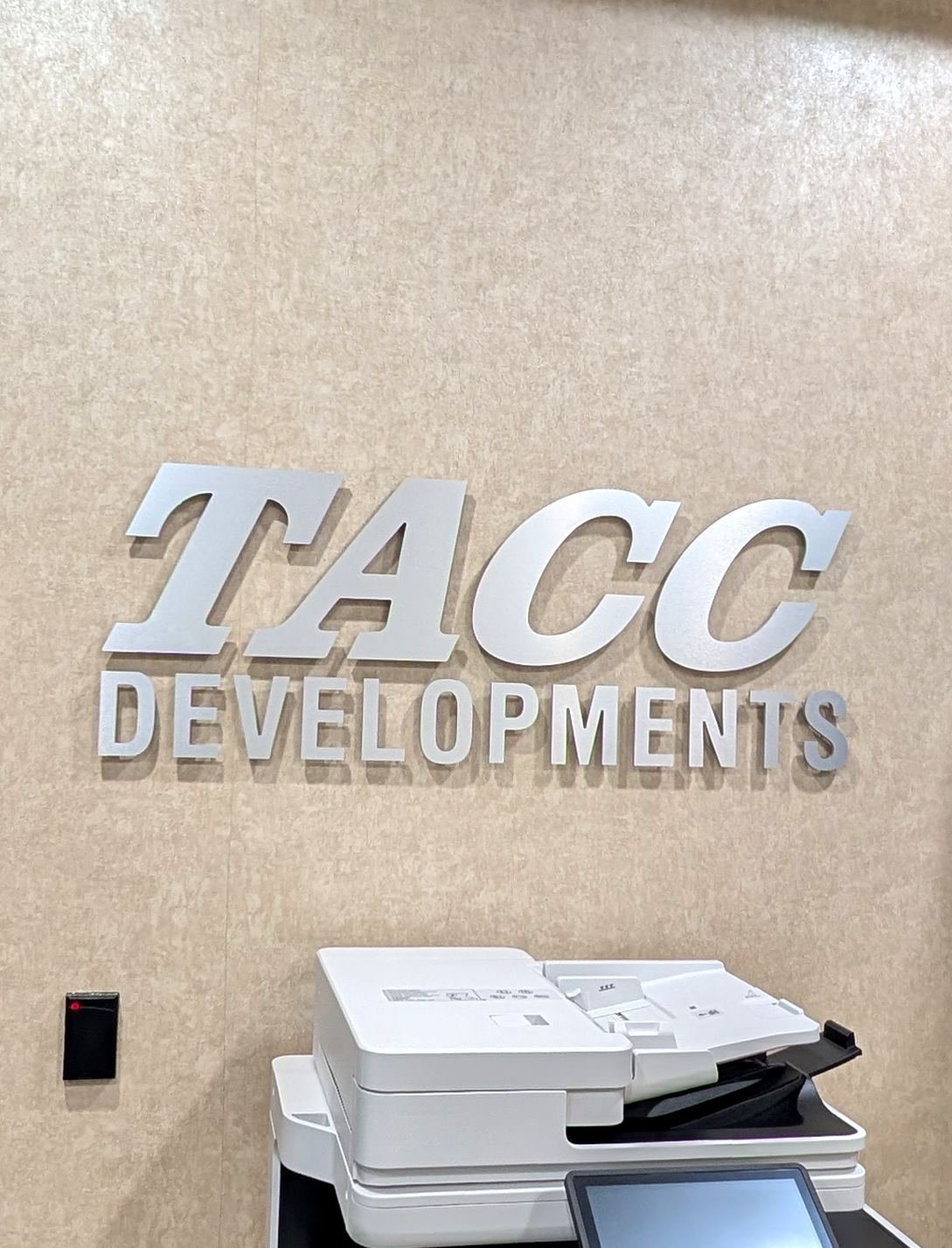 Brushed silver dimensional letters spelling TACC Developments mounted on an office wall.