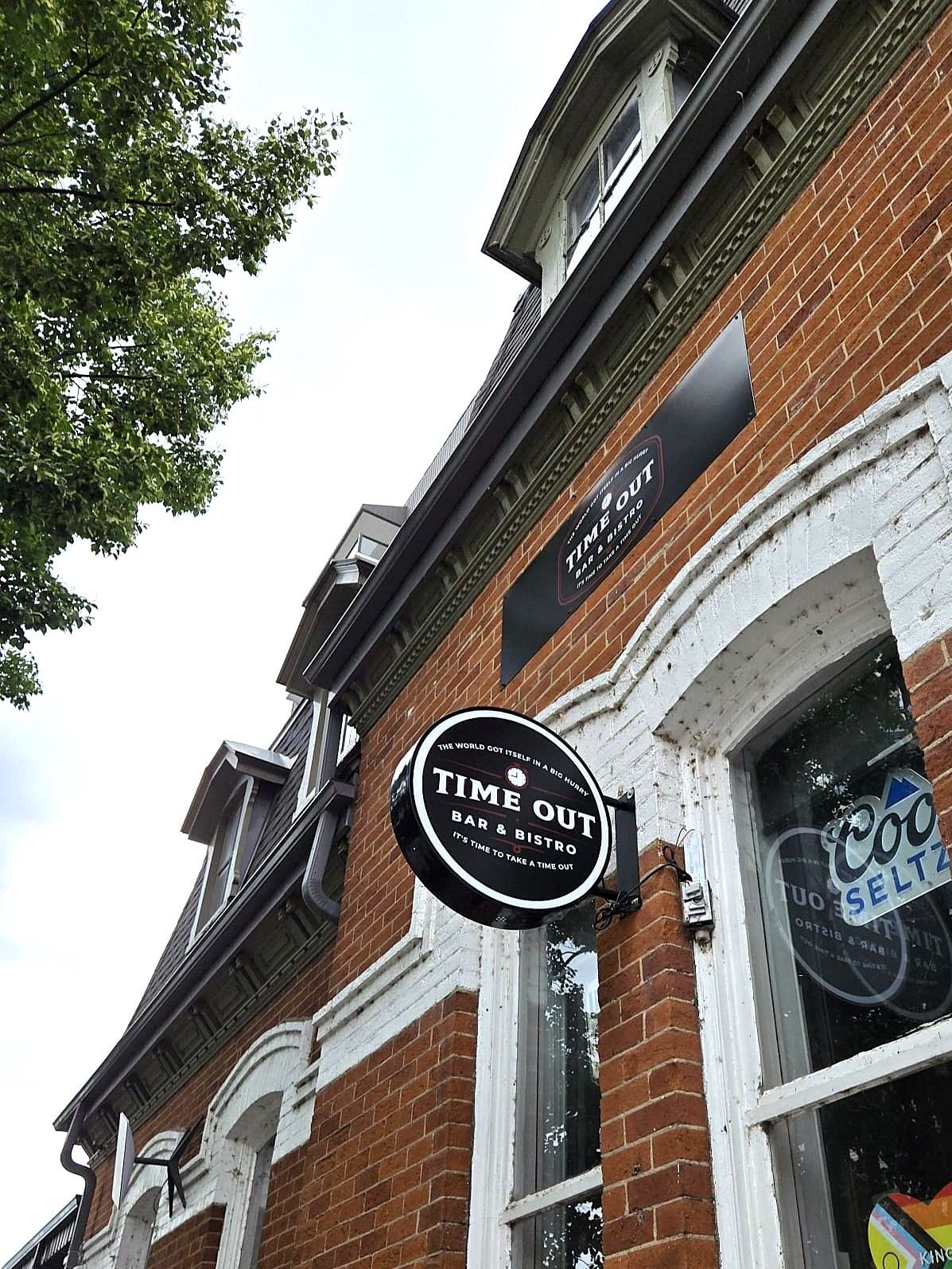 Round black Time Out Bar & Bistro sign hanging from a bracket on a red brick building